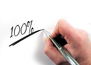 Mano escribiendo 100% en un papel, símbolo de recargo salarial