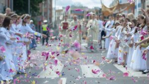 Procesión de Corpus Christi con niños lanzando pétalos de flores en la calle. Corpus Christi en RD: feriado legal,