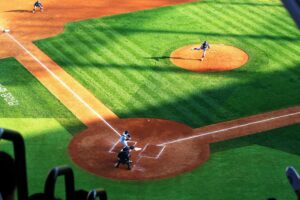 Vista aérea de un juego de béisbol en pleno lanzamiento, con bateador, receptor y pitcher en el diamante